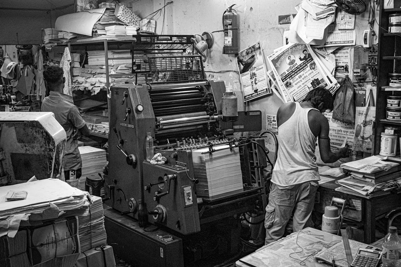 services-03 Black and white image of a bustling print shop with workers operating a printing press.